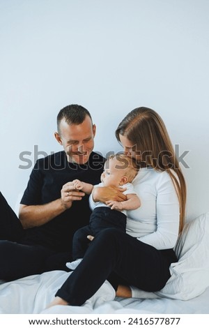 Young mother and father play with their newborn son lying in a white bed. A stylish family with a small child