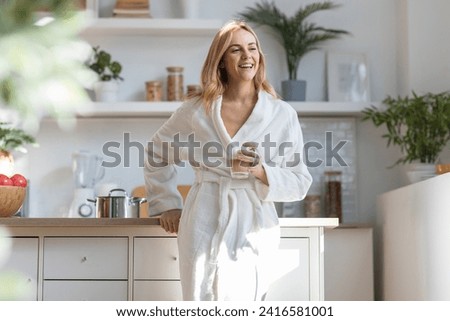 Shot of cute woman in bathrobe drinking a cup of coffee while looking forwards in the kitchen