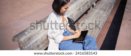 Portrait of young artist, asian girl drawing in digital tablet with graphic pen, sitting outdoors in park, getting inspiration.