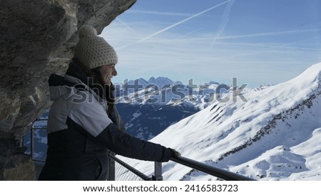 Woman posing for camera standing by handrail elevated metal support by cliffside with breathtaking view of mountains in background covered in snow
