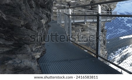 Metal pathway on side of mountain cliff, Grindelwald First Mountain trail pathway supported by elevated metal walkthrough in Swiss Alps Royalty-Free Stock Photo #2416583811