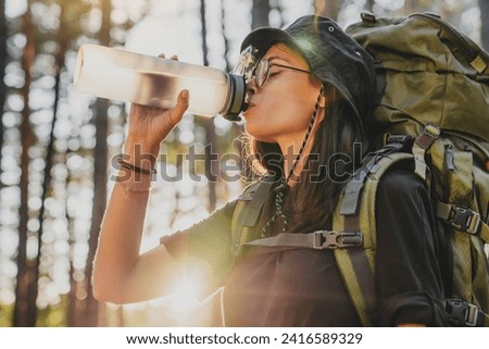 Profile photo of young woman drinking water in forest, sun flare. Female explorer traveler adventurer rehydrating with cold drink, relaxing feeling thirsty in solo trip