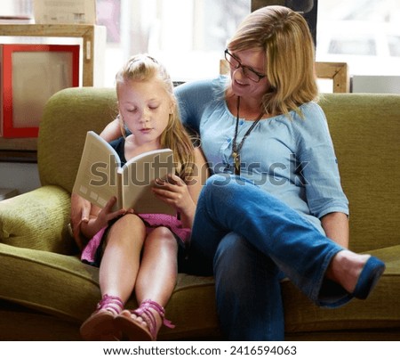 Reading with mom. A cute blonde girl and her mother reading on the couch at home.