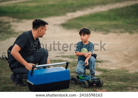 Young boy is crouching next to his toy car, feeling guilty for breaking it. He is looking at his father while the father is crouching next to a tool box. The father looks angry. Copy space. Royalty-Free Stock Photo #2416598163