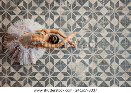Top view of gracious prima ballerina performing her art of dance at rustic and grungy place. Perfection of movements in rustic interior. Ballerina sitting on rustic geometric floor in abandoned place. Royalty-Free Stock Photo #2416598337