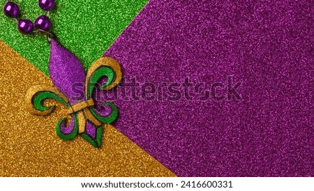 Mardi Gras beads with Fleur de lis, in glittering green, purple, and gold. Sparkling festive background for Mardi Gra in traditional colors. Royalty-Free Stock Photo #2416600331