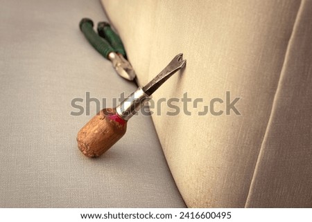 Work tools of an upholsterer. Staple remover resting on a sofa. Royalty-Free Stock Photo #2416600495
