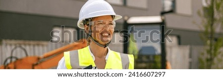 Smiling female construction worker in protective helmet standing against on construction background