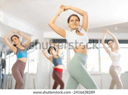 Smiling attractive slim young girl in enjoying passionate flamenco dance during group class in studio.. Royalty-Free Stock Photo #2416638289