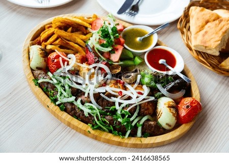 Dish with a appetizing assorty of Georgian cuisine of delicious shish kebab, french fries, baked vegetables, mushrooms,..peppers, fresh tomatoes, tkemali sauce, pita bread and sprinkled with chopped Royalty-Free Stock Photo #2416638565