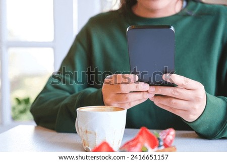 Closeup image of a young woman holding and using mobile phone in cafe