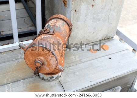 Old brown rusty fire hydrants beside fence on footpath, some scratched on surface of fire hose head, Thailand.