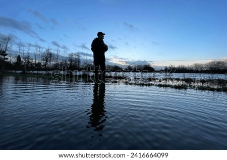 Exterior photo view of a adult male man who is looking alone at floods on field and road in Normandy during winter rains season during the day