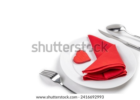 White plate with silverware of fork, knife, and spoon with red heart and red napkin isolated over white background. Romantic dinner Valentine's Day concept