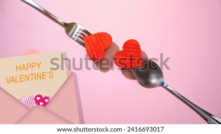 Silverware of fork and spoon with a red heart and valentine letter over pink background. Romantic dinner Valentine's Day concept
