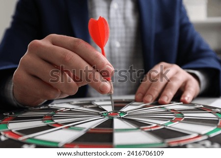 Business targeting concept. Man with dart aiming at dartboard at table, closeup