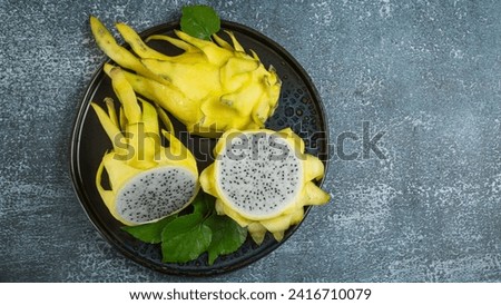 Top view. Bright yellow dragon fruit cut in half. White flesh. Delicious. Healthy fruit. There are vitamins in the black tray. on a gray background
