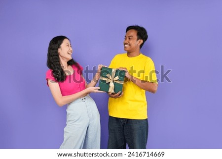 Photo of young Asian couple with gift box on purple background