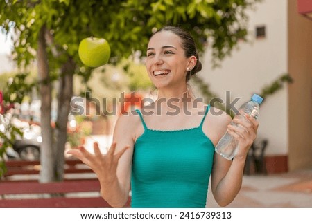 Young pretty woman at outdoors with an apple and with a bottle of water