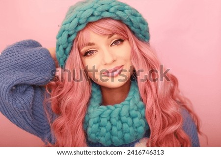 Cheerful girl in a knitted sweater and scarf smiles. pink hair. pink background