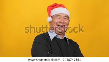 An old Asian man wearing a Santa hat smiling and looking at the camera. Isolated on yellow background in the studio.