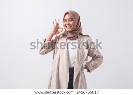 Portrait of excited Asian hijab woman in casual suit showing ok hand gesture and smiling looking at camera. Advertising concept. Isolated image on white background
