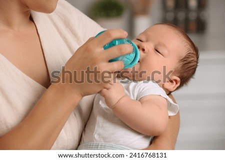 Mother feeding her cute child with infant formula indoors Royalty-Free Stock Photo #2416768131