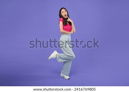 Full body of young asian woman open hands palm up holding something. Surprised happy female on isolated purple background. 