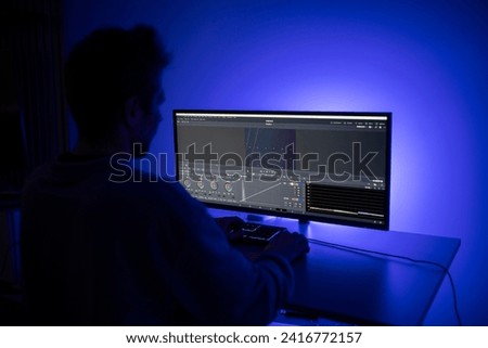 A video editor focuses intently on a complex editing software interface while adjusting content on a dual-screen workstation in a dark environment, illuminated by soft blue backlighting.