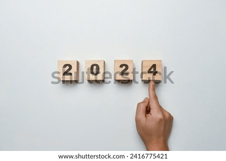 Hand pointing Wooden cube blocks with 2024 text on white background. Start new year and business vision concept