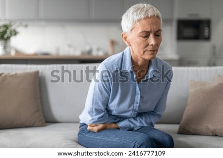 Unhappy Senior Woman Having Stomachache Suffering From Abdominal Pain Sitting On Sofa At Home. Mature Lady Having Painful Spasm Touching Belly. Stomach Diseases In Older Age Concept Royalty-Free Stock Photo #2416777109