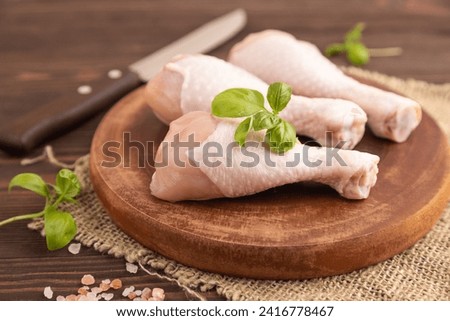 Raw chicken legs with herbs and spices on a wooden cutting board on a brown wooden background and linen textile. Side view, close up, selective focus Royalty-Free Stock Photo #2416778467