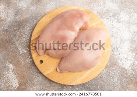 Raw chicken breast on a wooden cutting board on a brown concrete background. Top view, flat lay, close up. Royalty-Free Stock Photo #2416778501