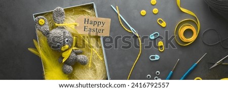 DIY Easter present making theme. Handmade knitted toy Easter rabbit in gift box, and needlework accessories on dark grey background. Overhead view, flat lay