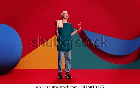 Vibrant image to promote cinema for young audience. Laughing young girl with popcorn and drink against abstract multicolored geometric background. Concept of entertainment, leisure activity, emotions Royalty-Free Stock Photo #2416810325