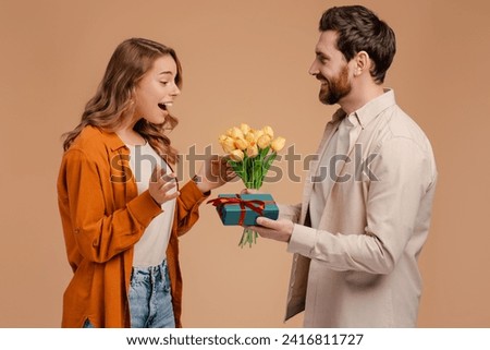 Handsome man make surprise for beautiful woman, holding gift and bunch of spring flowers isolated on background. Smiling young couple celebration birthday. love, dating concept