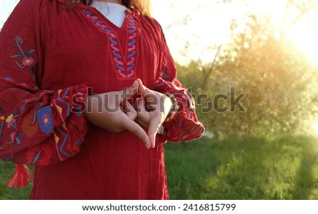 Woman on a red dress outdoor, doing meditation yoga mudra of hands, yoni symbol. female adi shakti hand gesture. spiritual, tantric practice, meditation. female energy, health concept.