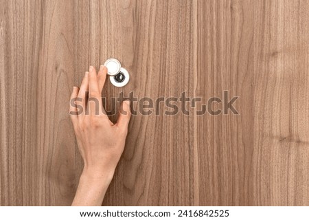 Close up view of woman hand opening metal peephole cover on wooden door when somebody knocking to apartment. Woman stay alone at home. Concept of privacy, safety and protection Royalty-Free Stock Photo #2416842525