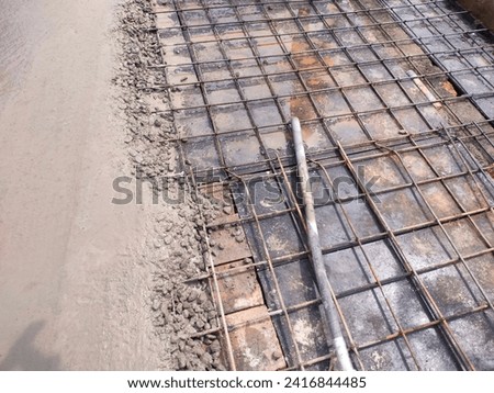 Close-up of wet concrete poured, levelled portion and steel reinforcement bar design on other half hd hi-res jpg stock image landscape photo, top ankle view selective focus.(steel bars tied up seen).