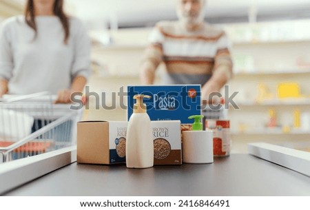 Groceries on the checkout counter conveyor belt and customers waiting in the background Royalty-Free Stock Photo #2416846491