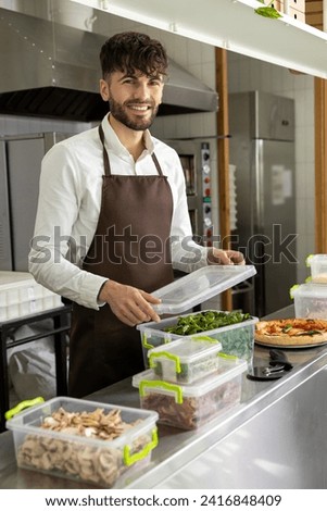 Dark-haired bearded young pizzeria worker packing food into containers