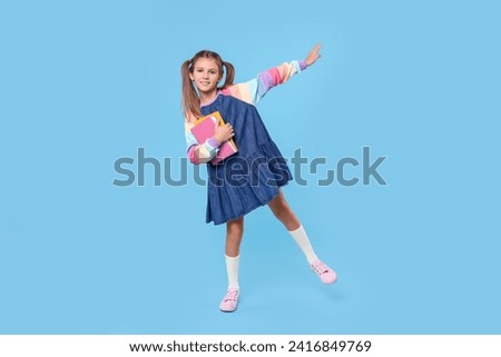 Smiling schoolgirl with books on light blue background Royalty-Free Stock Photo #2416849769