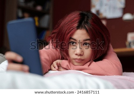 Teenage girl with smartphone taking selfie before posting it in social networks while lying on bed in front of camera at leisure