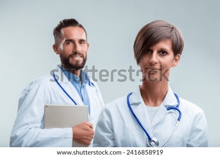 Professional medical team, woman at forefront exhibits expertise, man with tablet supports in the background Royalty-Free Stock Photo #2416858919