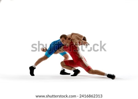 Two strong and skilled wrestlers in blue and red wrestling uniform are wrestling and doing grapple against white studio background. Concept of fair wrestling, championship, win competition.
