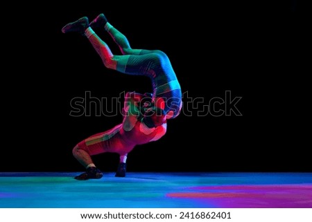 Two young man, professional sportsman of freestyle wrestling in uniform fighting against black background in mixed neon lights. Concept of motion, action, combat sports, strength and power, movement.