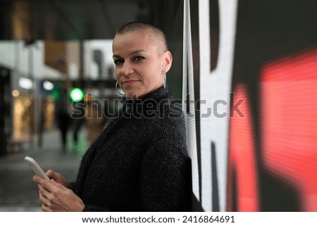 bald shaved young adult woman posing with neon lights in the city looking at camera and smiling for her good health
