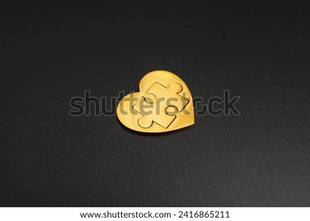 Golden heart with a puzzle piece nestled inside, set on a dramatic black backdrop. Unity, completeness, and love related concept. Royalty-Free Stock Photo #2416865211