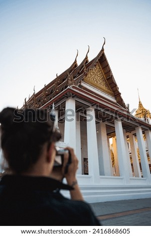 (Selective focus) A defocused tourist is taking pictures at the Wat Ratchanatdaram, a beautiful Buddhist temple that stands proud in the heart of downtown Bangkok, Thailand.
