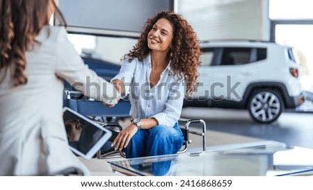 Happy woman buying a car and closing the deal with a handshake with the saleswoman at the dealership. Smiling car saleswoman discussing a contract with a female customer.